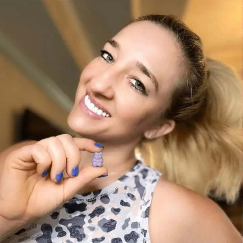 Woman holding a grape-flavored sleep gummy, smiling and showcasing the product for better rest and relaxation.